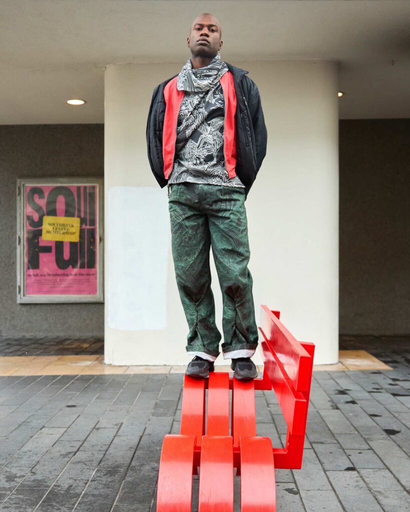 Folu Odimayo stands atop a red bench in London, UK