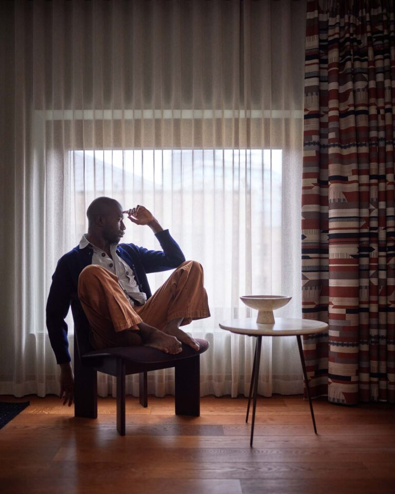 Folu Odimayo models contemporary British clothing in front of a window in his room at the Sir Devonshire Square Hotel in London, UK