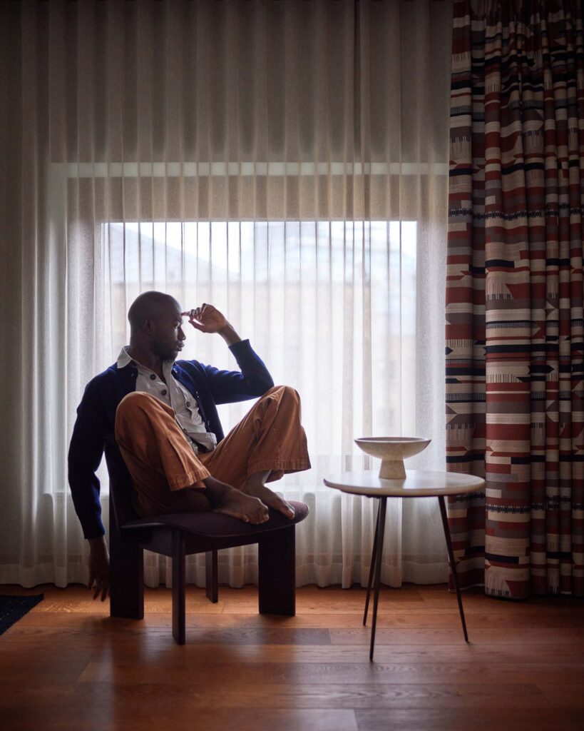Folu Odimayo models contemporary British clothing in front of a window in his room at the Sir Devonshire Square Hotel in London, UK