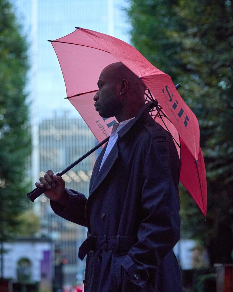 Folu Odimayo holding a red umbrella by Sir Hotels in London, UK