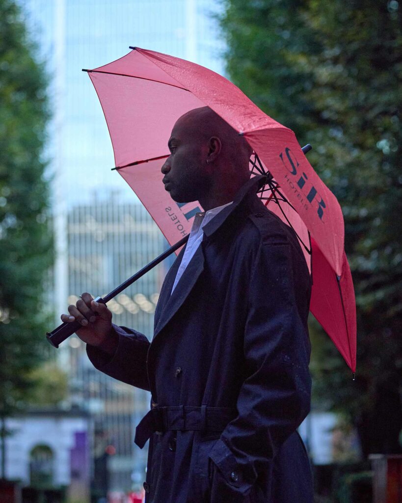 Folu Odimayo holding a red umbrella by Sir Hotels in London, UK