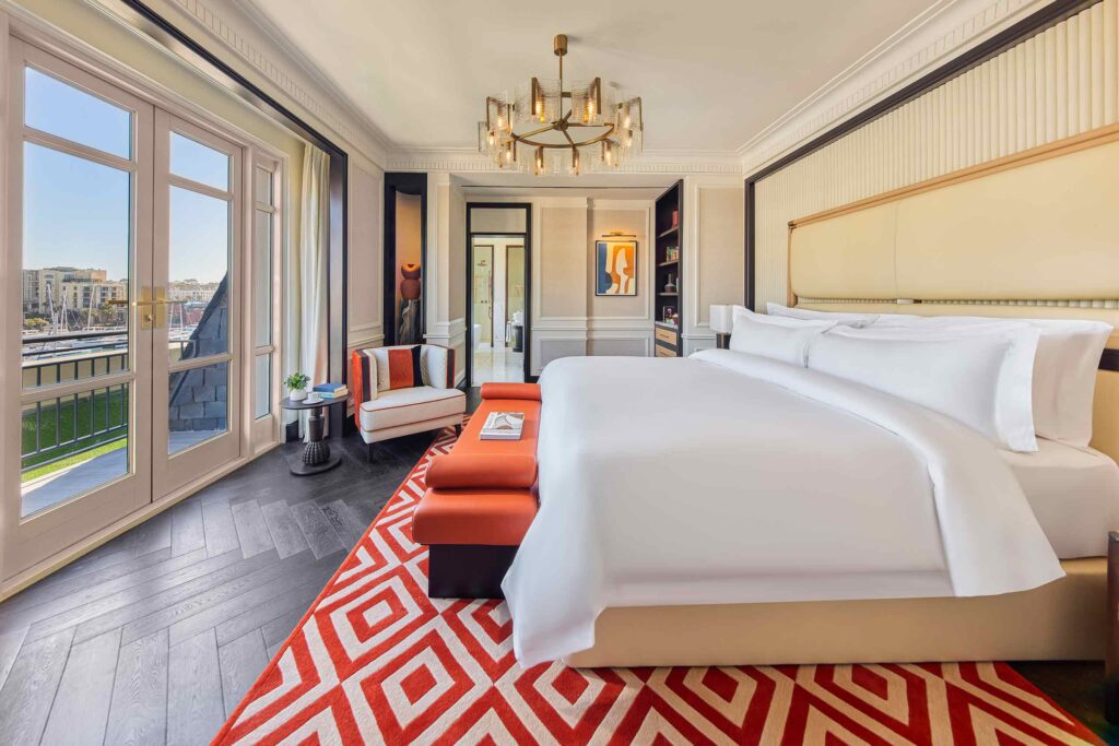 Suite bedroom interiors at Cape Grace, red diamond carpets, colourful interior decor and art and a super king bed, looking out to a terrace