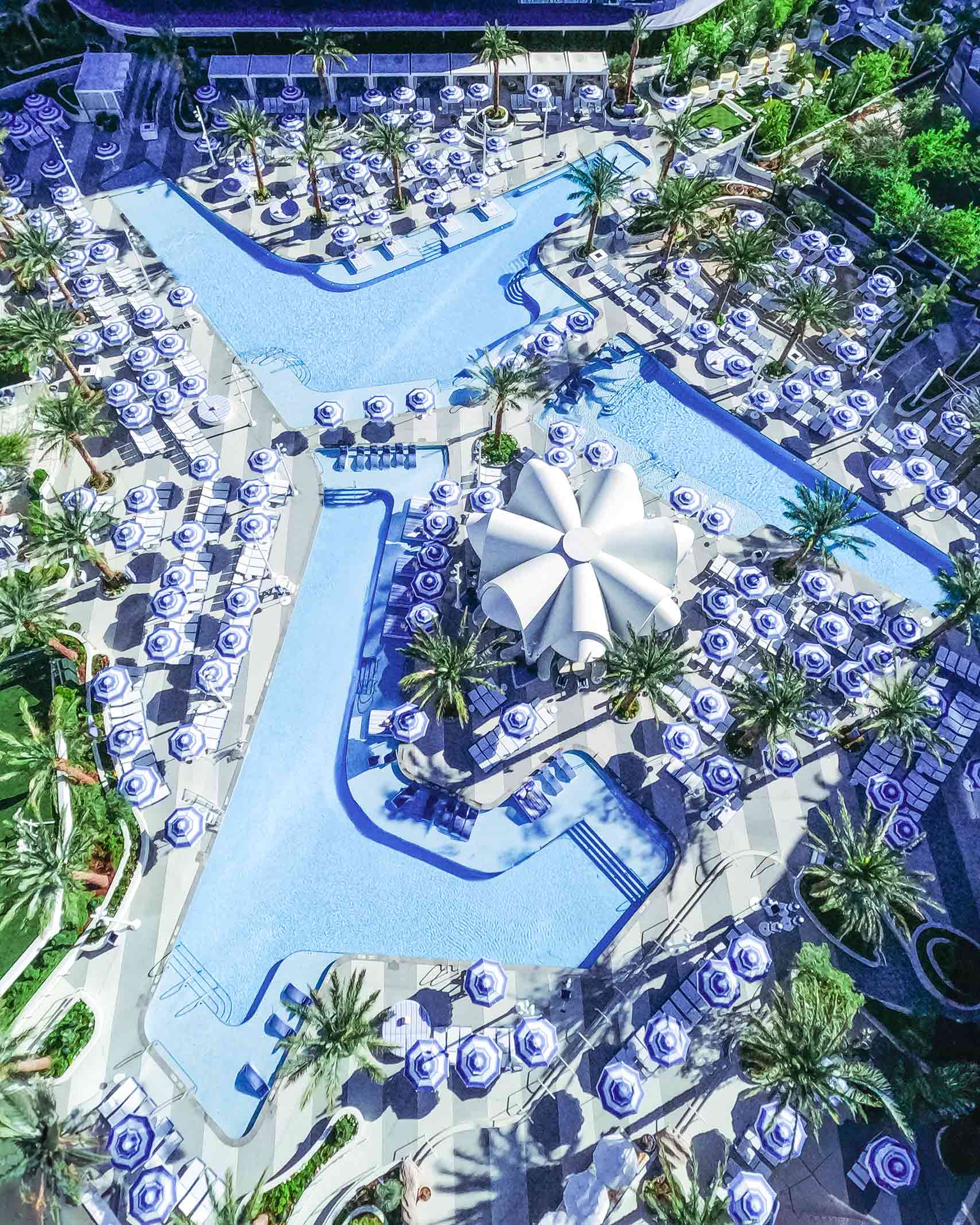 Birdseye view of the 6-acre Oasis Pool Deck at the Fontainebleau Las Vegas, with its conch like central structure and blue umbrellas
