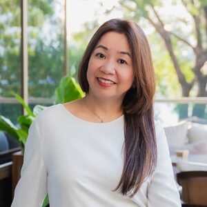 Portrait of Josephine Png, Area Director of Sales and Marketing, Capella Ubud and Capella Bangkok. Josephine is a Singaporean Chinese woman with long brown hair. She wears a simple necklace and white dress