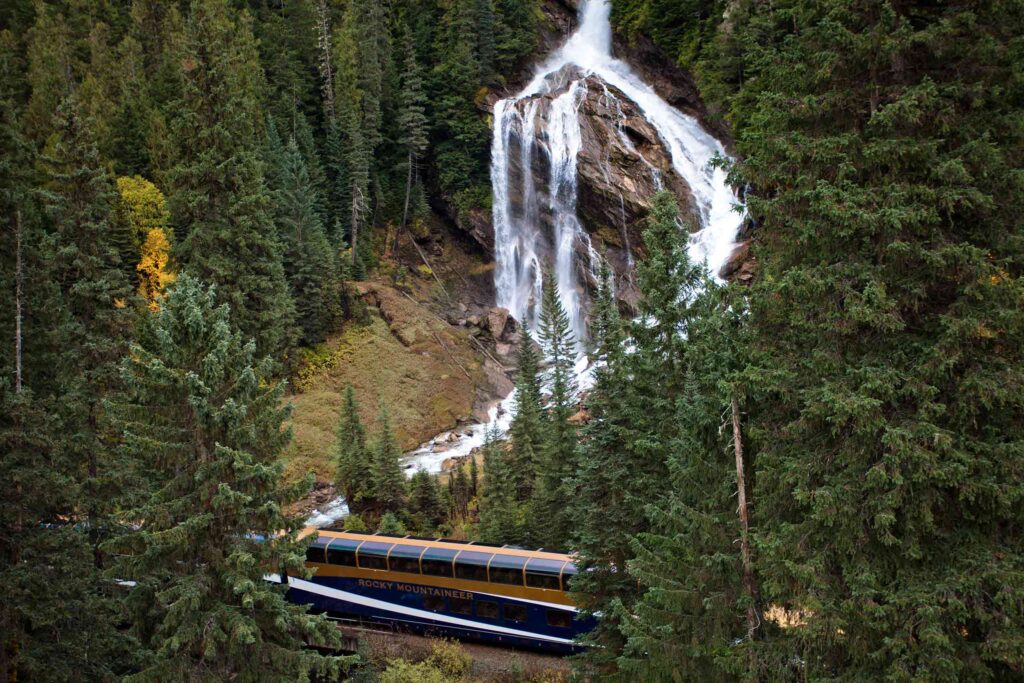 A glimpse of the Rocky Mountaineer in front of a majestic waterfall in British Columbia, Canada