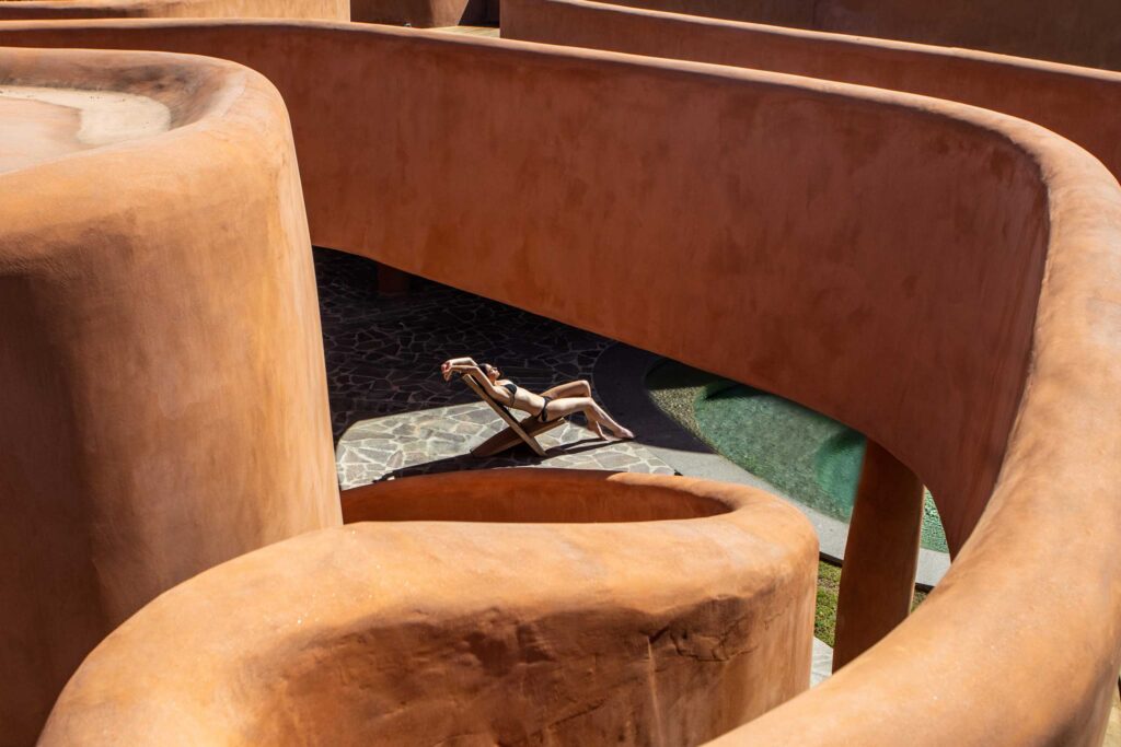 A woman in a bikini sunbathes amid the curves of the orange Villas at Is Molas, Sardinia