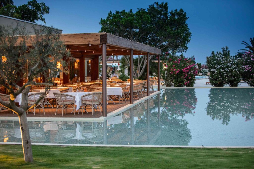 Pool restaurant at Is Molas Resort Sardinia, dining table flank a shallow pool dotted with trees
