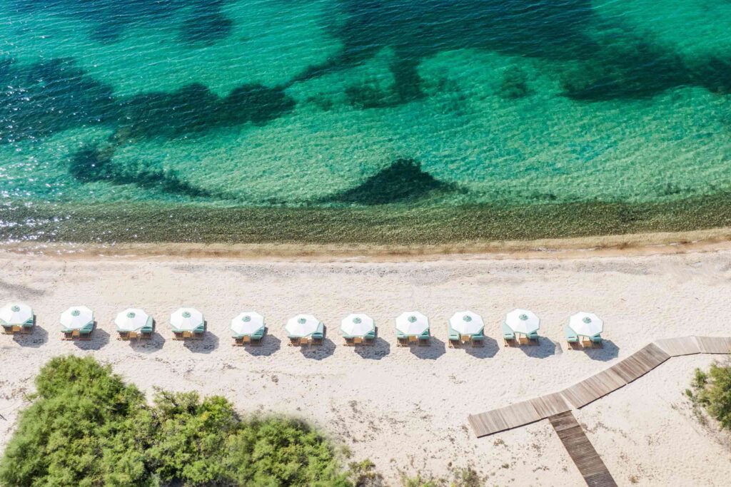 Turquoise and white sun parasols sit on the sand looking out to the blue green Mediterranean Sea
