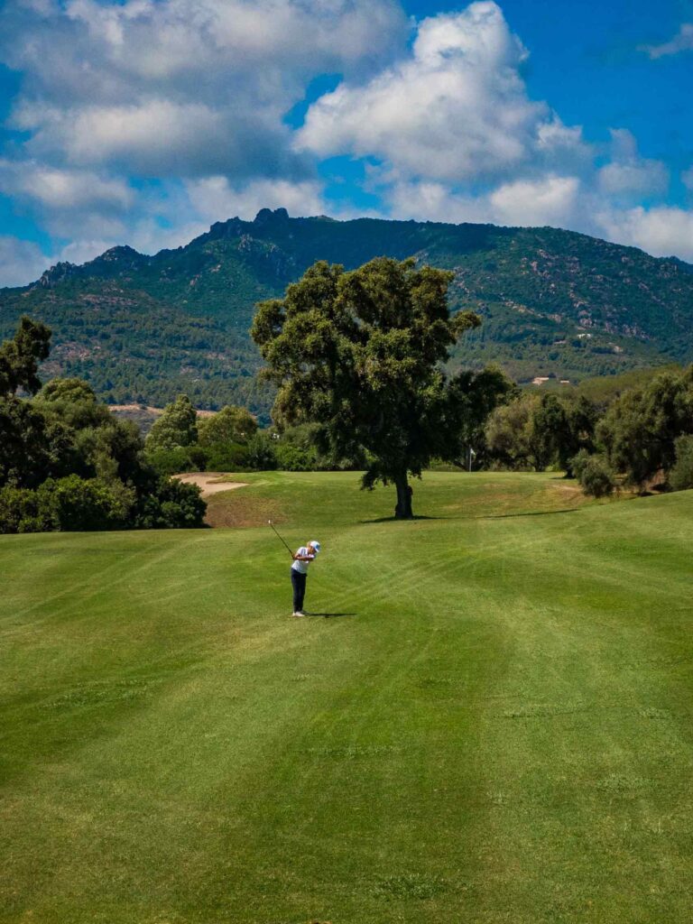 Female golfer at Is Molas golf course, playing on a green with trees and mountains in the background