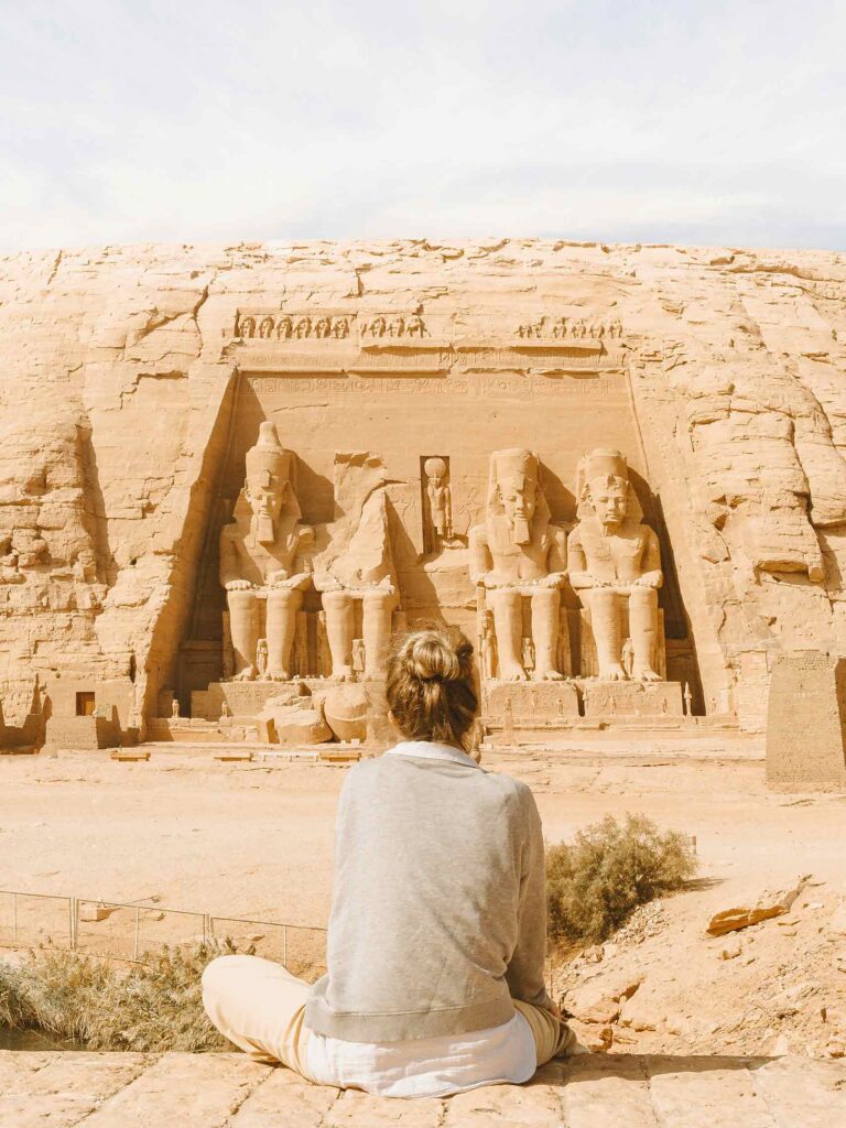 A blonde woman in beige sits and stars at the entrance to a tomb in Egypt