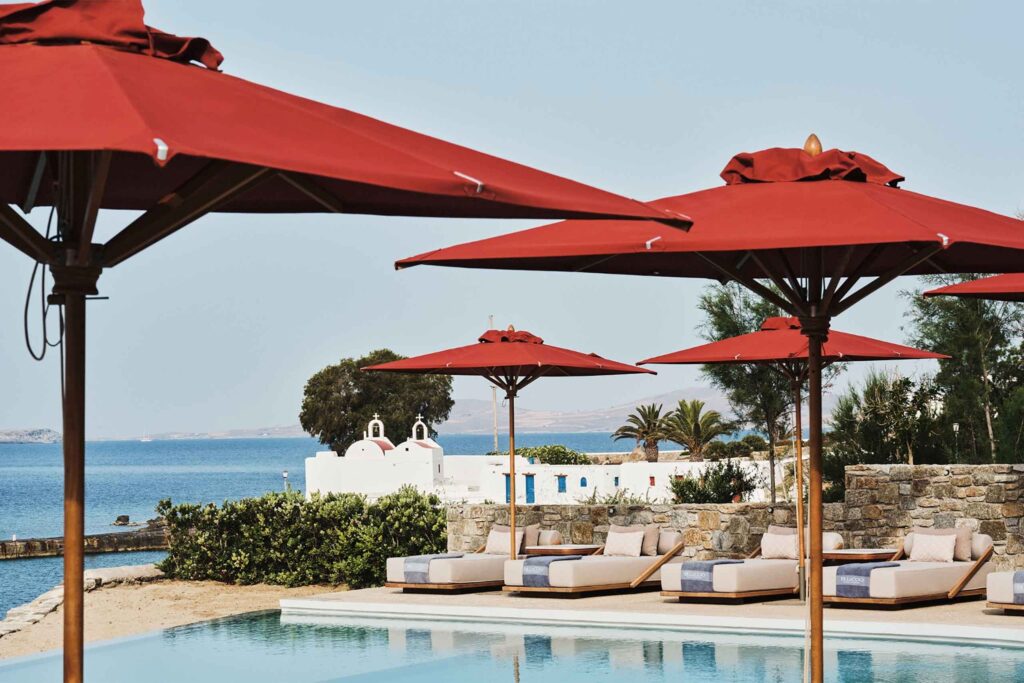 Poolside at The Coast at Bill & Coo, Mykonos, infinity pool overlooking the sea and church, punctuated with burnt sienna parasols
