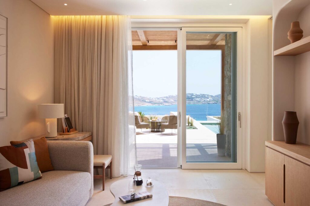 Calm, neutral Interior of suites at The Coast Bill & Coo looking out through glass forrs to the patio, pool and sea beyond