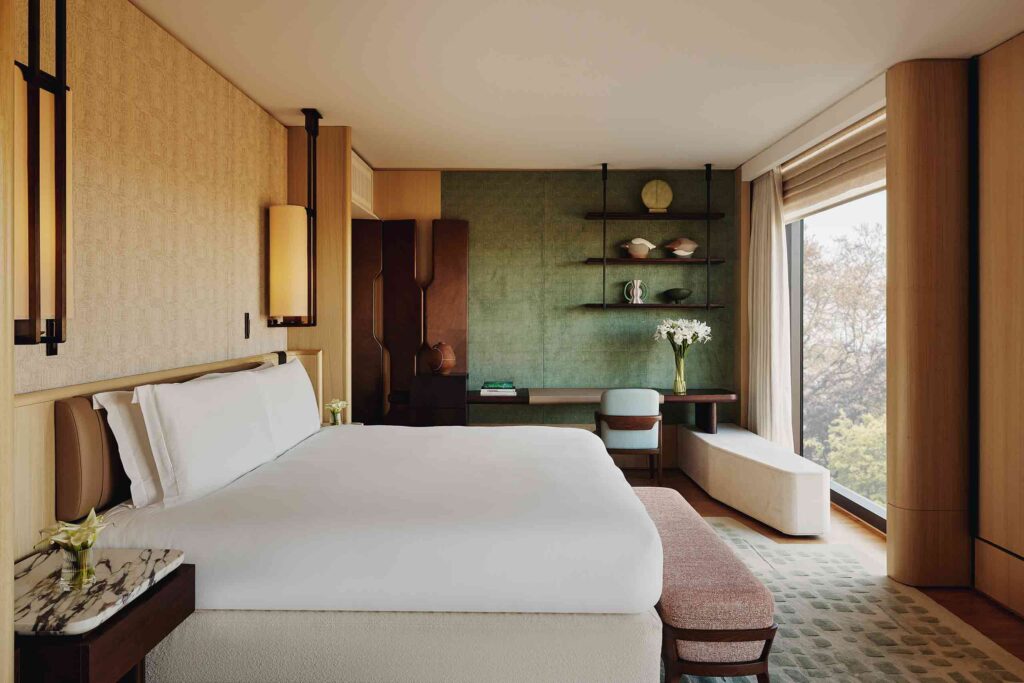 Andre Fu designed suite bedroom featuring honey coloured wood panelling, bespoke cabinets and rust coloured sofa looking out over Hyde Park at The Emory, London