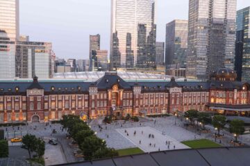 Exterior shot of the red-brick, Gothic Revival architecture The Tokyo Station Hotel, set to a backdrop of tall, glass skycrapers in Japan