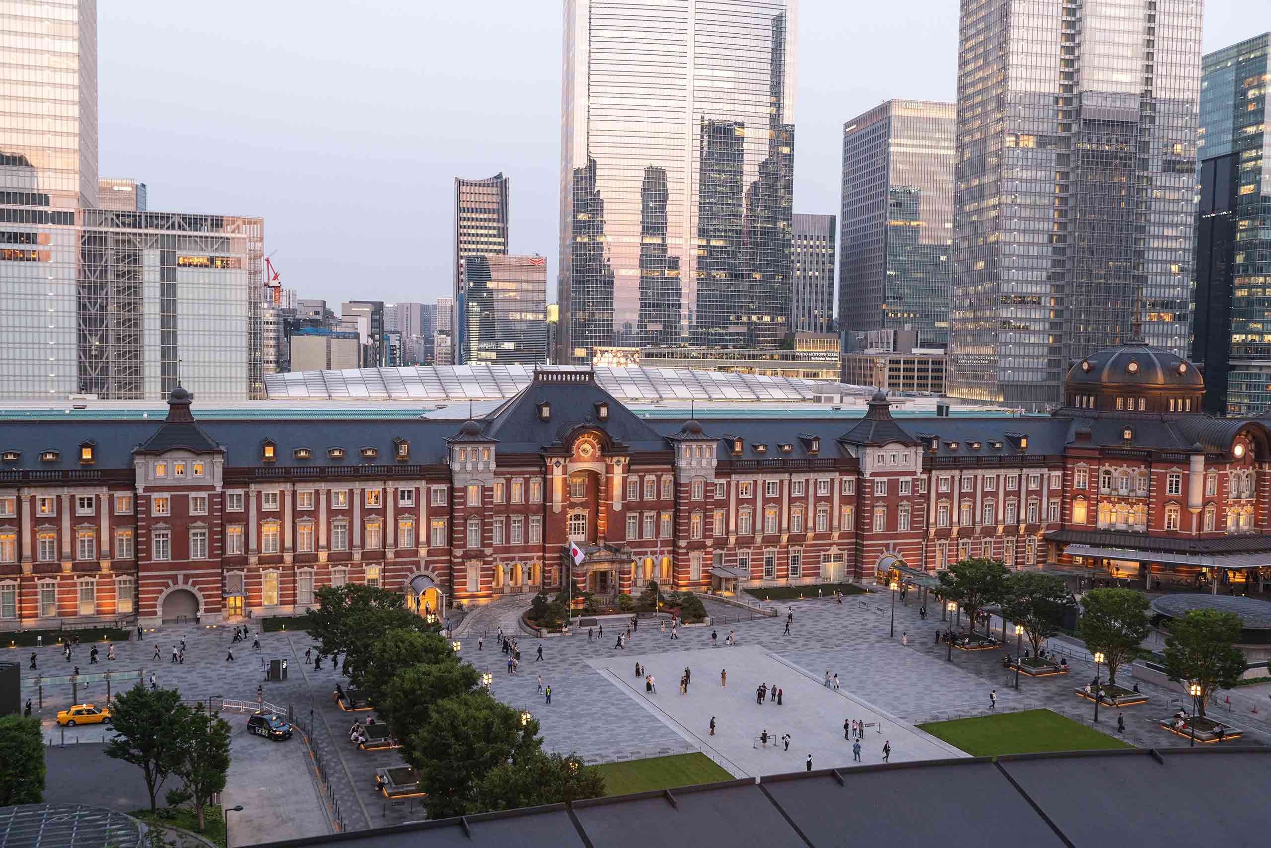 Exterior shot of the red-brick, Gothic Revival architecture The Tokyo Station Hotel, set to a backdrop of tall, glass skycrapers in Japan