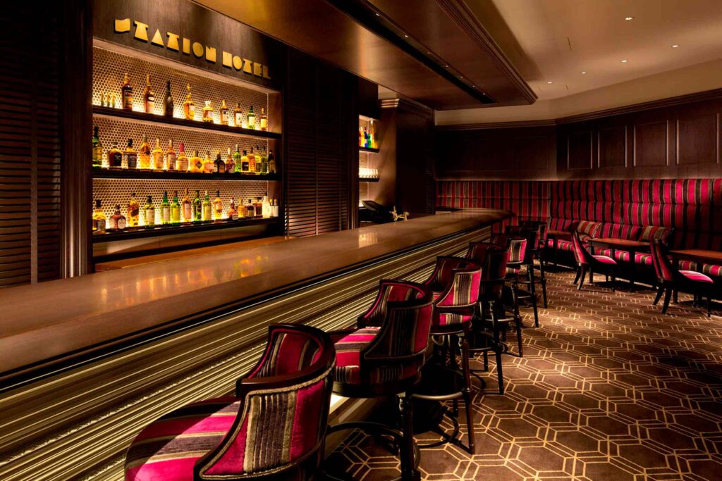 Interior shot of the Bar and Cafe Carmelia at the Tokyo Station Hotel, with its retro signage, wood paneled walls, and bar with red and brown striped bar stools