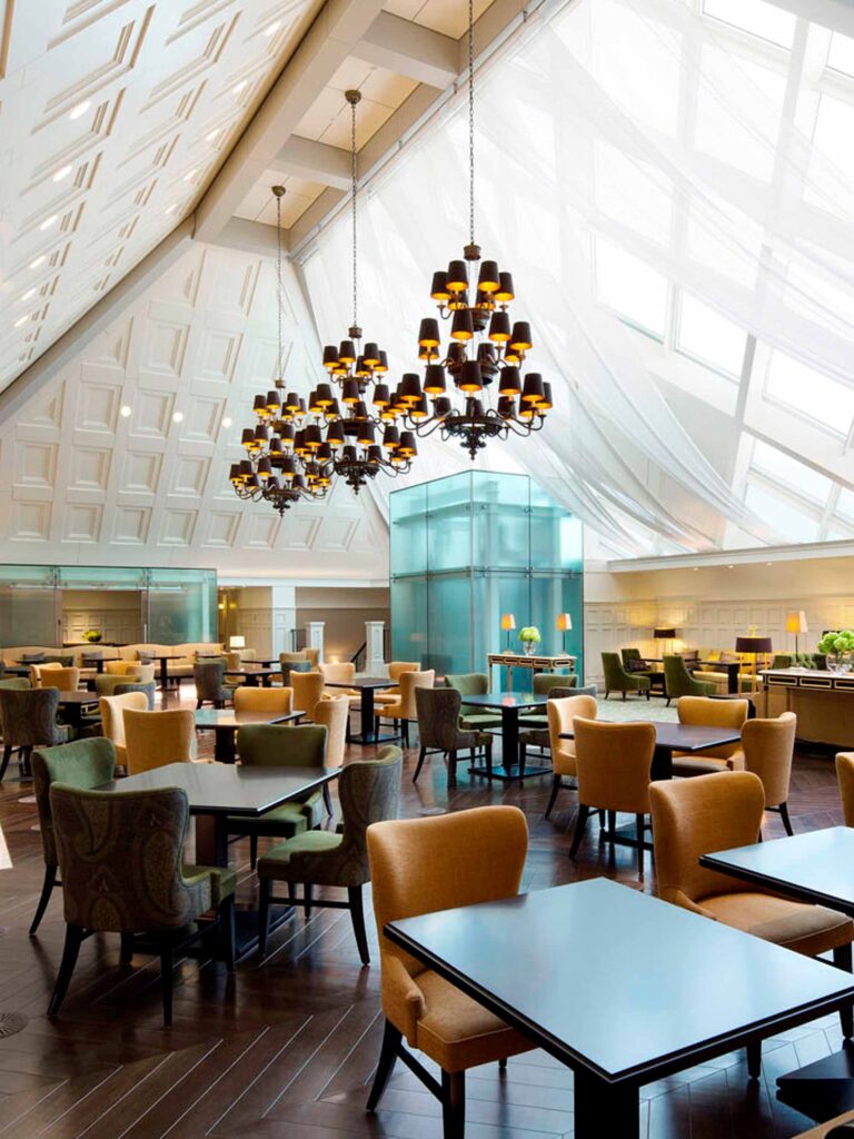 Interior shot of the atrium dining room at the Tokyo Station Hotel, with its high pitched roofs and chandeliers. Beneath them, dining tables and chairs