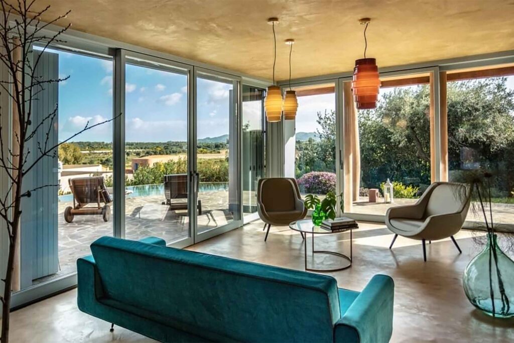 Interiors of Villas at Is Molas, Sardinia – blue sofa, stone armchairs, Murano glass lanterns looking out through floor to ceiling windows to pool and garden