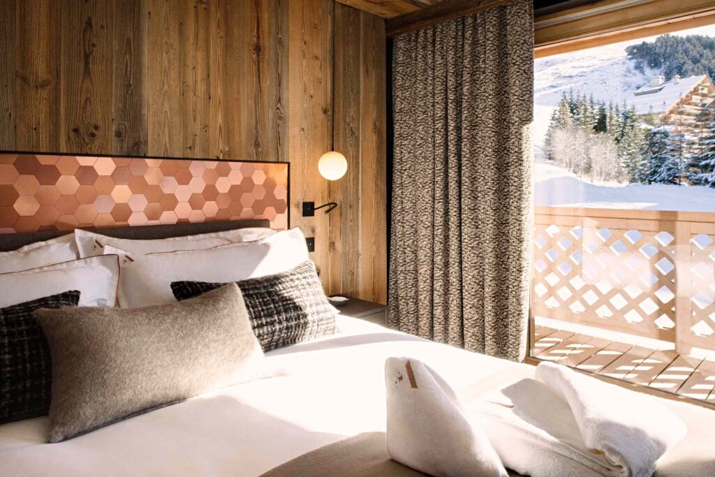 A bed decked in pillows and throws next to a window offering a view of a winter landscape