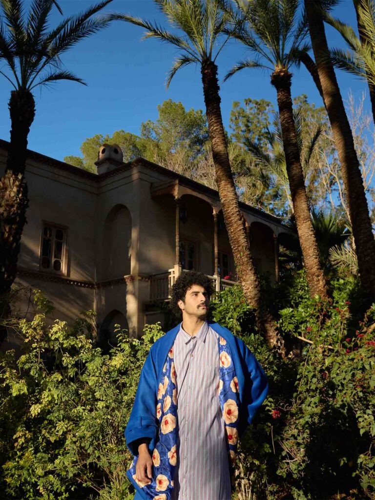 Amran Bennaji wearing a cotton shirt and a cashmere-wool coat in front of palm trees in Marrakech, Morocco