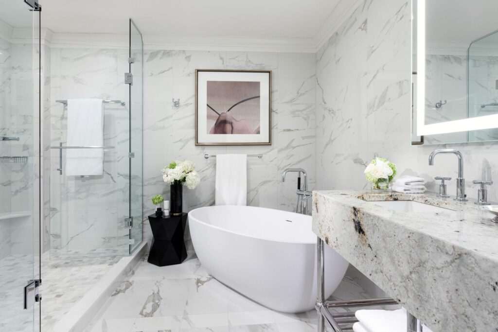 A white bathtub next to a walk-in shower in a white marble-effect bathroom at Fairmont Hotel Vancouver, Canada