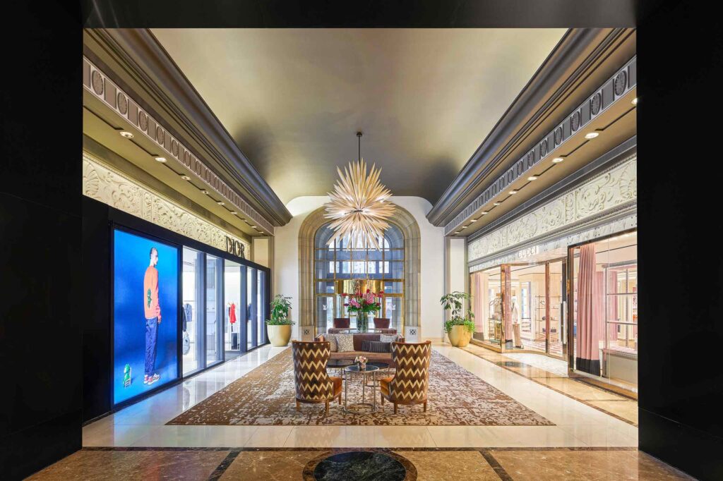 A shopping passage with a Gucci store across from a Dior boutique, with an elegant seating arrangement between them