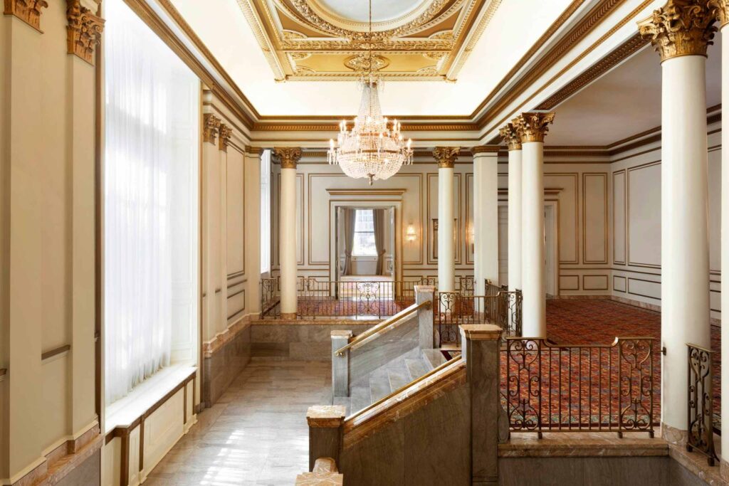 A grand, historic staircase at whose centre a large chandelier offers an elegant focal point