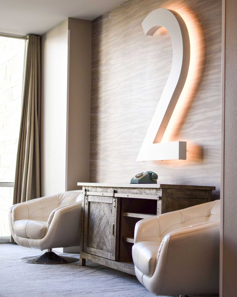 The lift lobby area of Hotel Paseo, with a sideboard, 2 chairs a vintage blue telephone and an enormous number 2 on the wall designating the floor