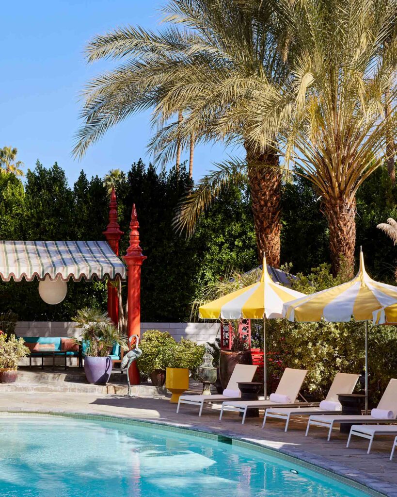 Pool area at Parker Palm Springs, with landscaped palms, yellow and white striped parasols and matching deckchairs