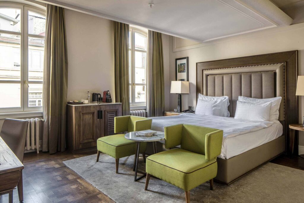 Stylish pistachio-green chairs at the end of a king-size bed inside a room at The Bank Hotel Istanbul, a Member of Design Hotels, Istanbul, Türkiye