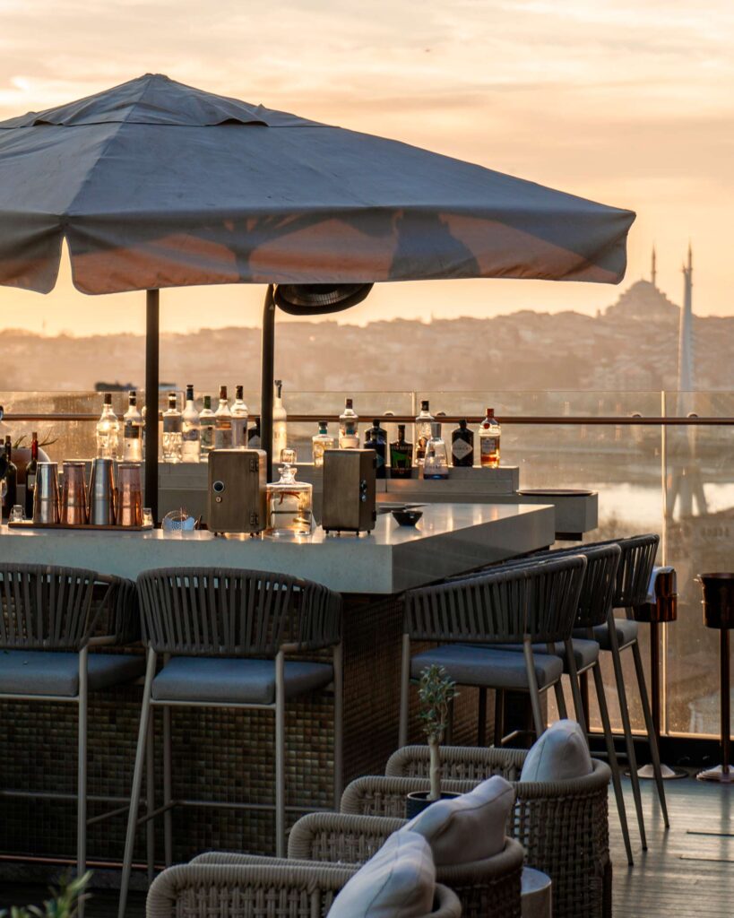 A parasol over a bar counter in front of the sunset in Istanbul at the Rooftop Bar at The Bank Hotel Istanbul, a Member of Design Hotels, Istanbul, Türkiye