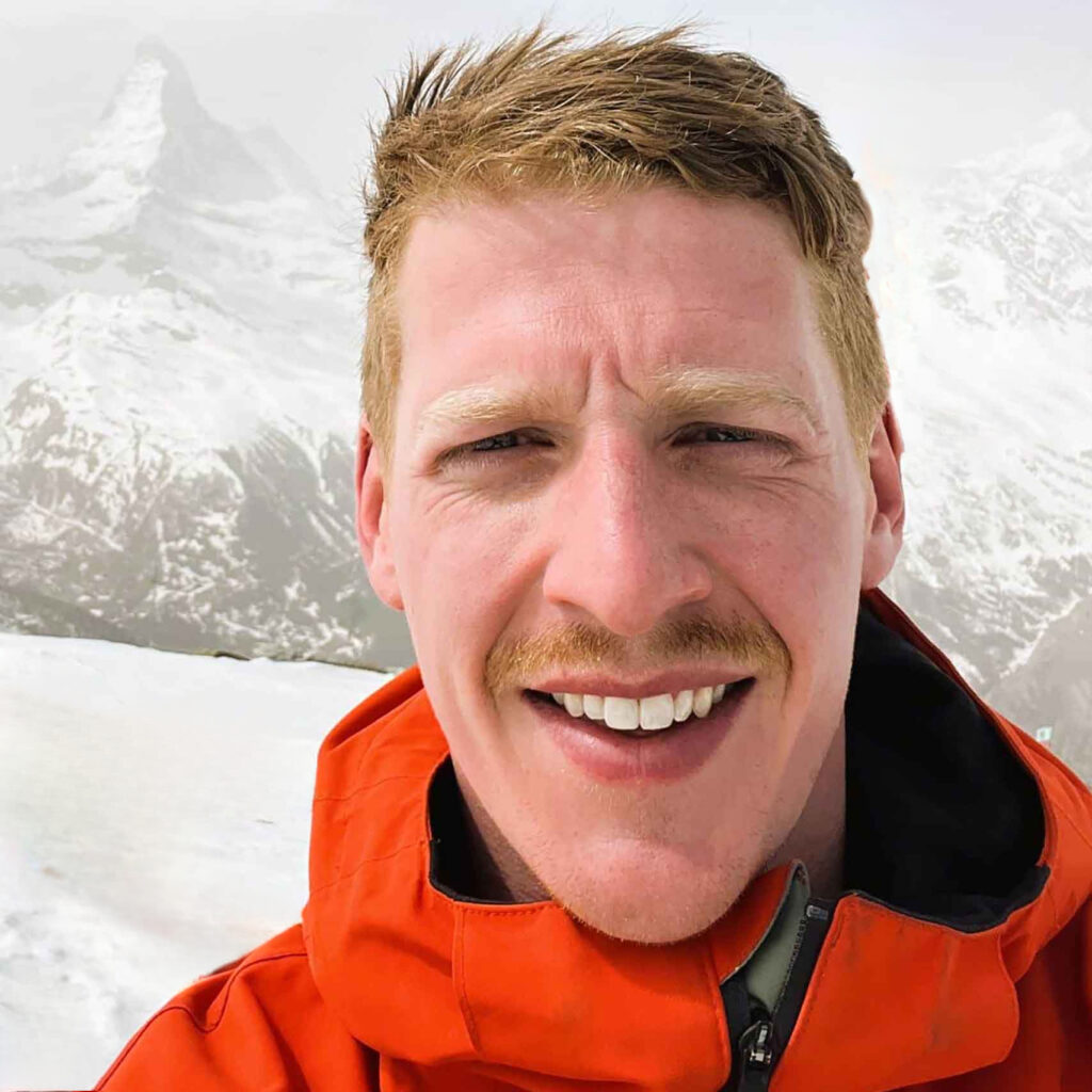 The Luxury Chalet Company founder Cameron Temple on the piste. He is a white man, with blonde hair and moustache and is wearing a red ski jacket