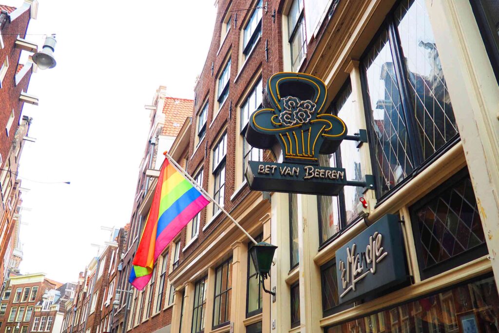 The outside of Café 't Mandje in Amsterdam, with a rainbow flag and a large neon sign featuring the name of its historical founder, Bet van Beeren