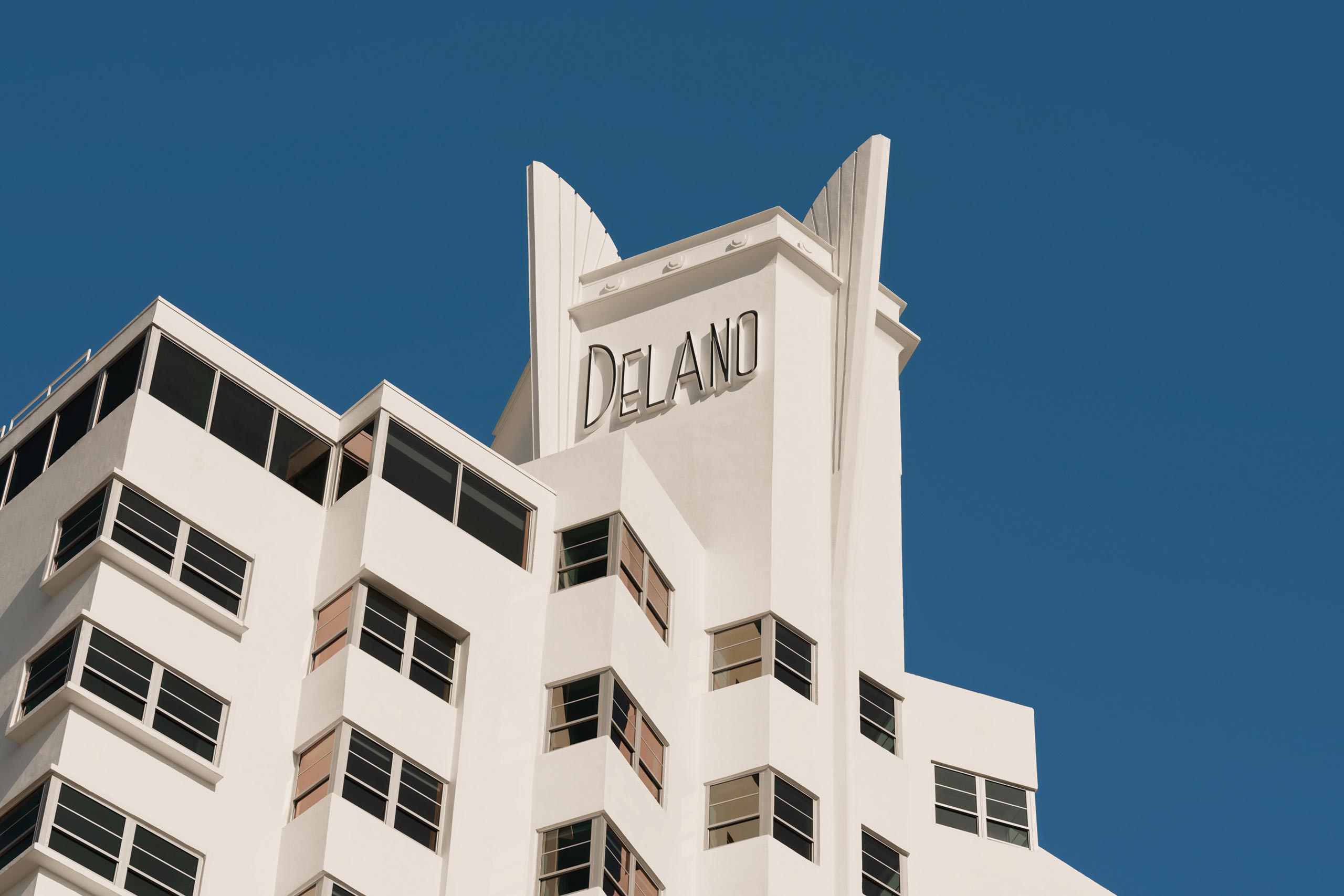 Whitewashed Miami Modernism architectural flourishs of the exterior of the Delano Miami Beach against a clear blue sky