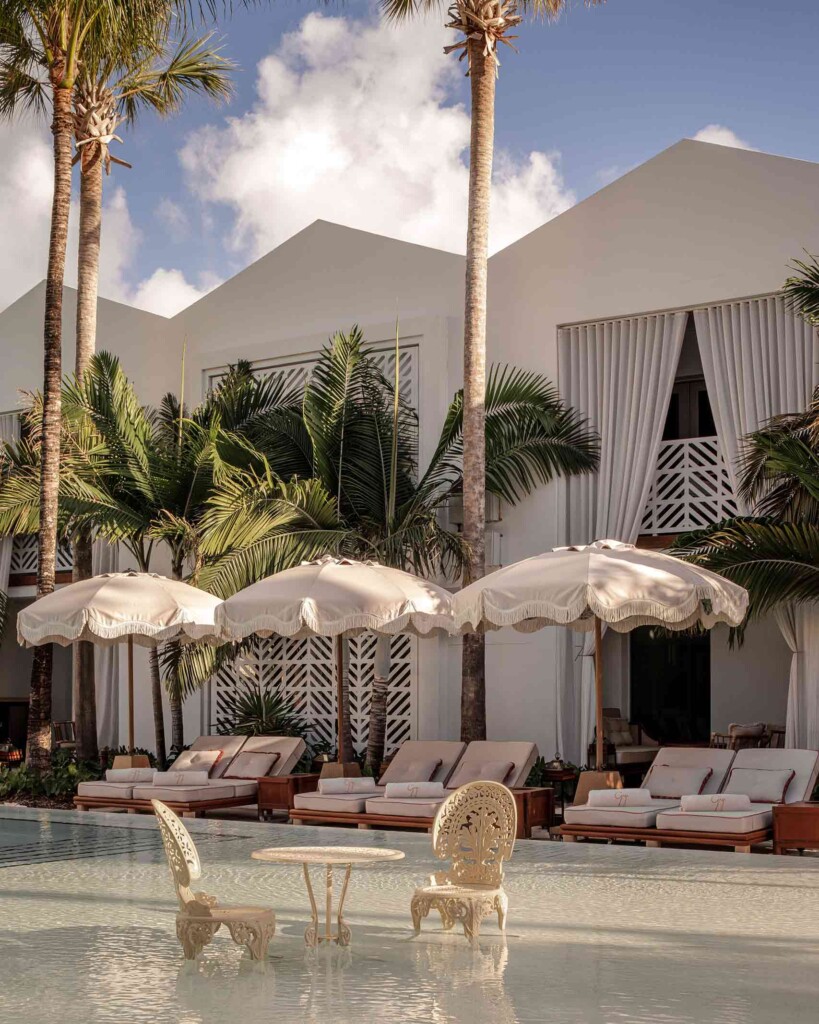 View of white, wrought iron garden chairs and tables in the pool overlooking sunloungers and bungalows at the Delano Miami Beach