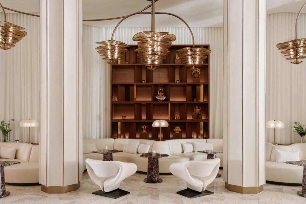 Common areas of the Delano Miami Beach, with restored architectural flourishes (hexagonal columns), contemporary glass lighting, white furnishing and a wooden shelf adorned with art