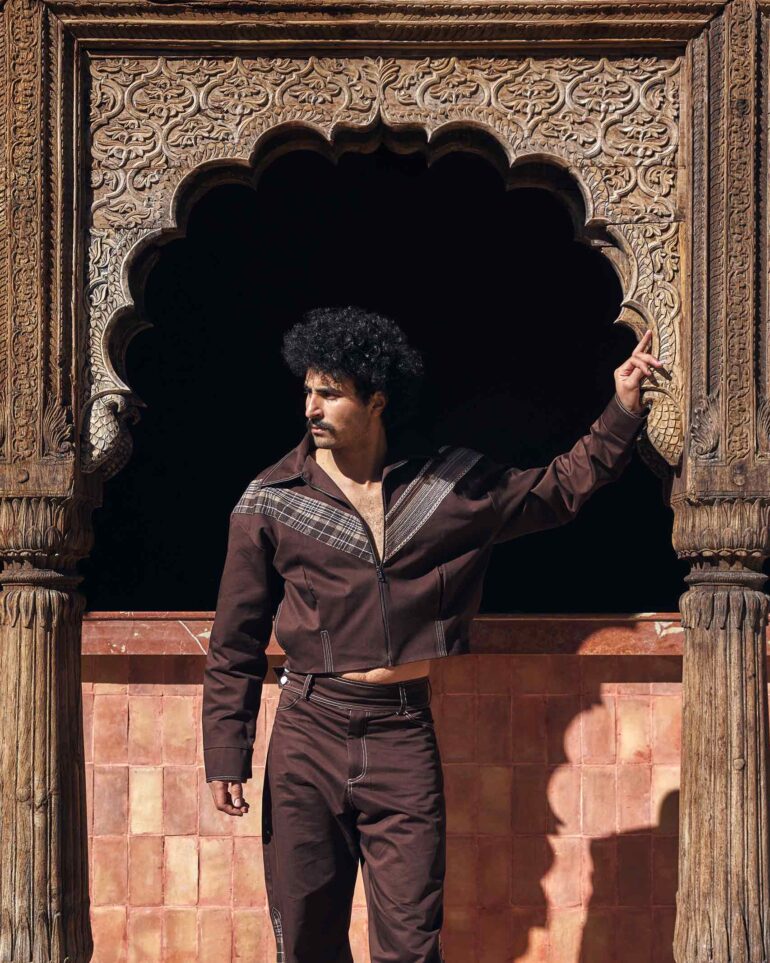 Amran Bennaji wearing a brown unisex jacket while standing beneath a carved, wooden doorframe in Marrakech, Morocco