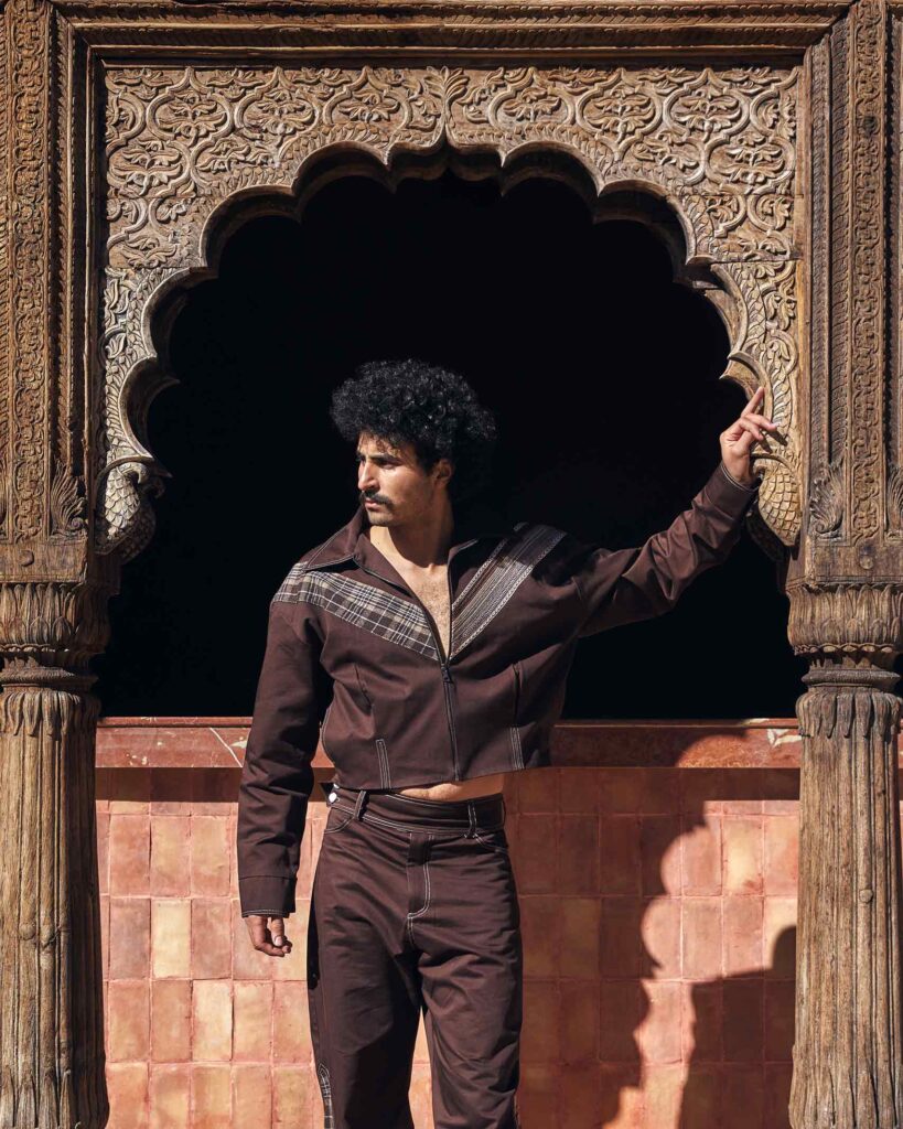 Amran Bennaji wearing a brown unisex jacket while standing beneath a carved, wooden doorframe in Marrakech, Morocco