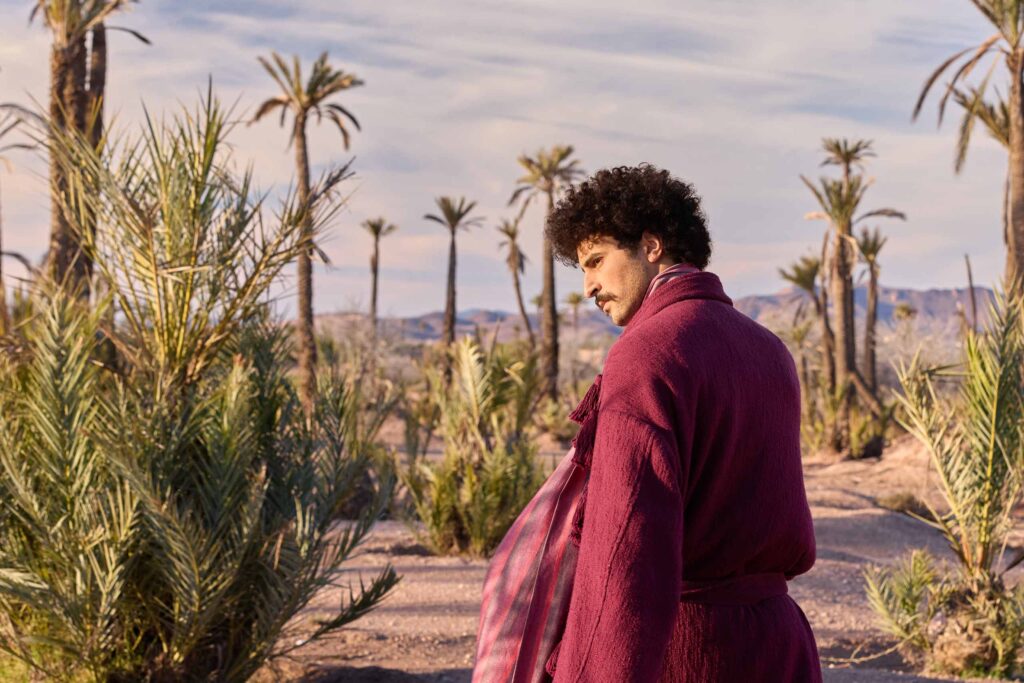 Amran Bennaji wearing a cotton scarf blouse and looking over his shoulder while surrounded by palm trees in Marrakech, Morocco