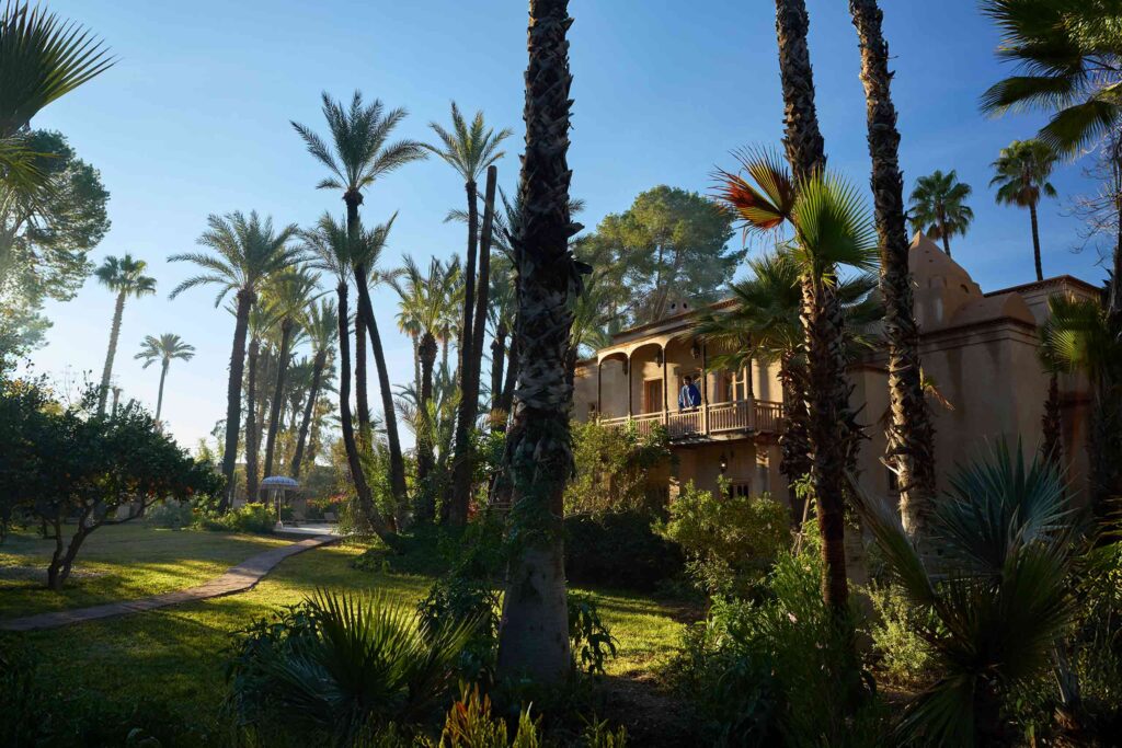 Amran Bennaji wearing a cotton shirt and a cashmere-wool coat while stood on a balcony at Jnane Rumi in Marrakech, Morocco