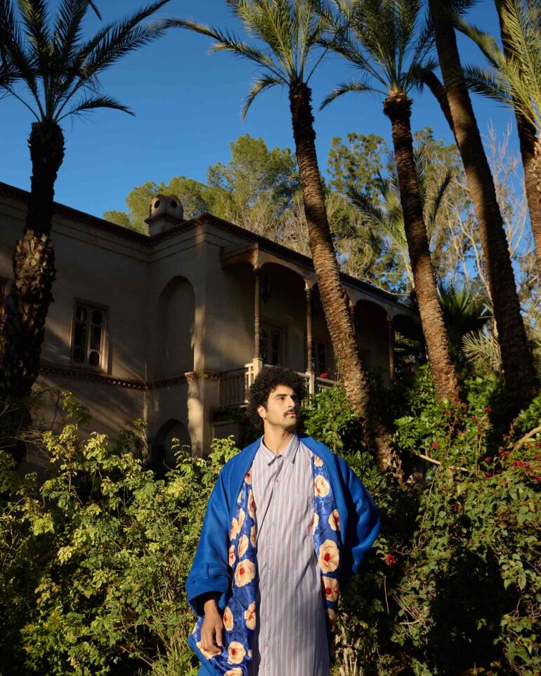 Amran Bennaji wearing a cotton shirt and a cashmere-wool coat in front of palm trees in Marrakech, Morocco