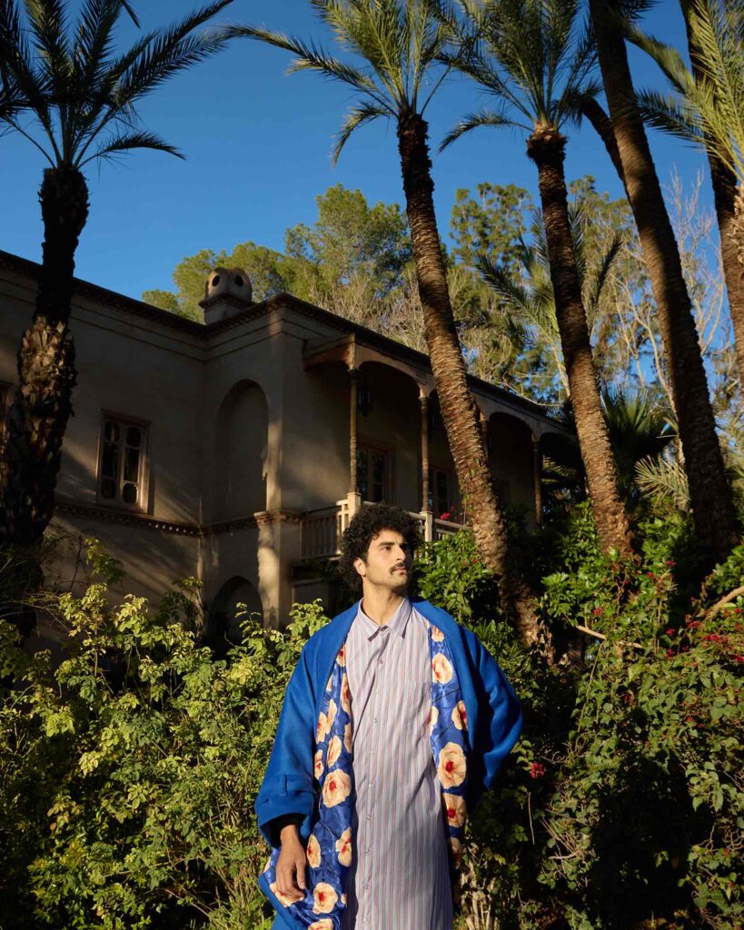 Amran Bennaji wearing a cotton shirt and a cashmere-wool coat in front of palm trees in Marrakech, Morocco