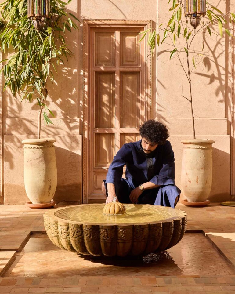 Amran Bennaji wears a navy 'Nomad' coat while playing with a water feature in Marrakech, Morocco