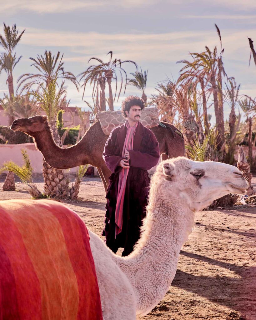 Amran Bennaji wearing a cotton scarf blouse while surrounded by palm trees and camels in Marrakech, Morocco