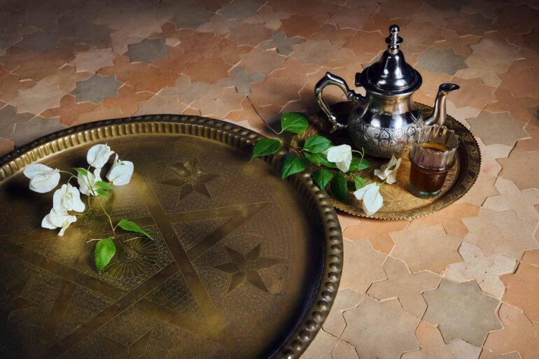 A silver Moroccan tea pot and a golden tray with flowers on it on a tiled floor in Marrakech, Morocco