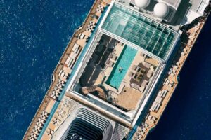 Aerial shot of Explora Journeys ship showing the open, retractable roof of the pool deck, with a man lying back in the pool beneath it