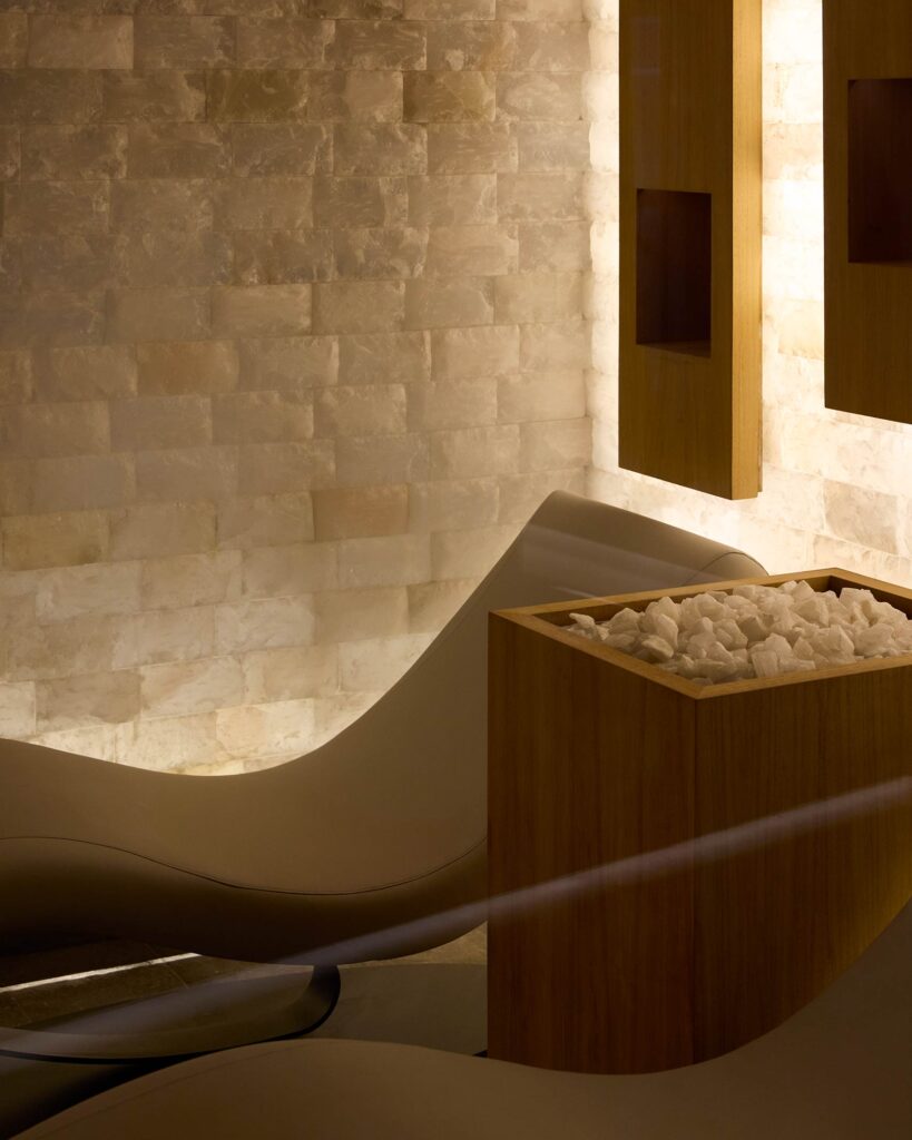 White Himalayan salt wall and curved relaxation chairs in a dimly lit spa on an Explora Journey ship