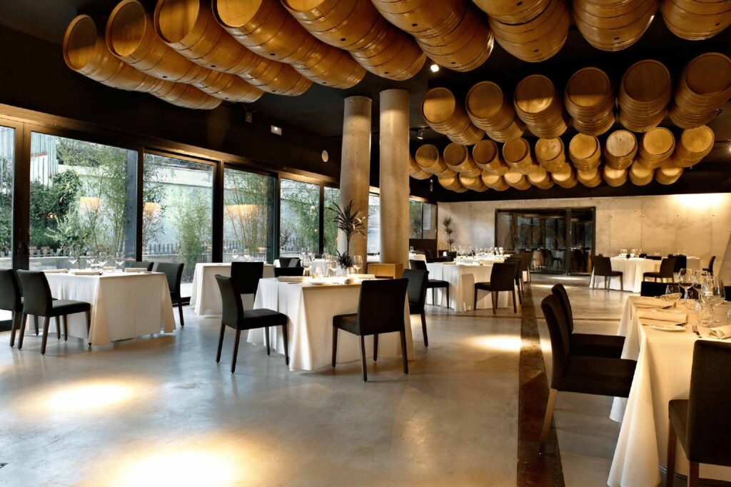 Contemporary restaurant at Hotel Viura with wooden wine barrels suspended from the ceiling, minimalist tables and floor-to-ceiling windows.