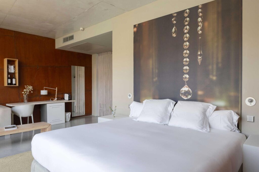 Spacious guest room at Hotel Viura with king bed, neutral tones, modern furnishings and large photographic wall art.