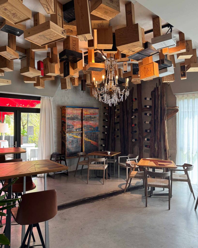Lounge area with suspended wine crates ceiling, chandelier lighting and rustic wood tables.
